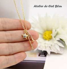 a person holding a gold necklace with a star on the bottom and a white flower in the background