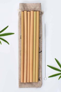 bamboo straws are lined up in a pouch next to some green leaves on a white surface