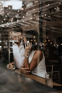 a man and woman sitting at a bar talking on their cell phones