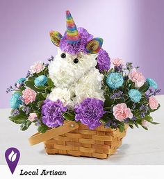 a stuffed unicorn is sitting in a basket with purple and white flowers on the table