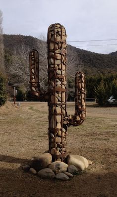 a large cactus sculpture sitting in the middle of a field next to rocks and trees