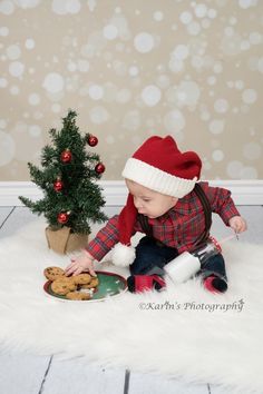 a baby in a santa hat is playing with some cookies near a small christmas tree