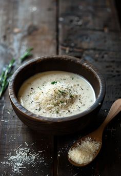 a wooden bowl filled with soup and parmesan sprinkles next to a spoon