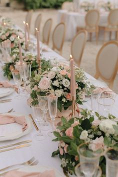 a long table is set with pink and white flowers, greenery, and candles