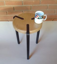 a coffee cup sitting on top of a wooden table next to a brick wall with black legs