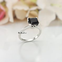 a black diamond ring sitting on top of a white table with flowers in the background