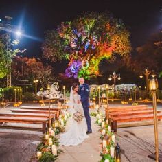 a bride and groom standing in front of candles at their outdoor wedding ceremony with an illuminated tree behind them