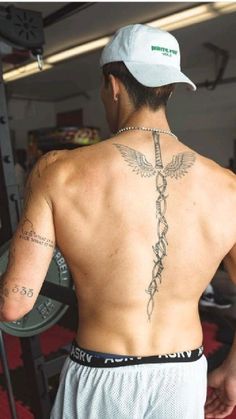 a man with a cross tattoo on his back is standing in front of a barbell