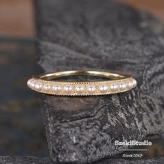 a gold wedding band with pearls on the side and beaded edge, sitting on a rock