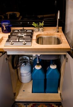 a small kitchen with a sink, stove and two blue containers under the counter top