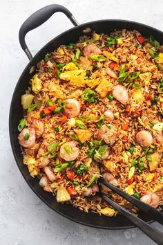 a skillet filled with rice and shrimp on top of a white table next to a fork