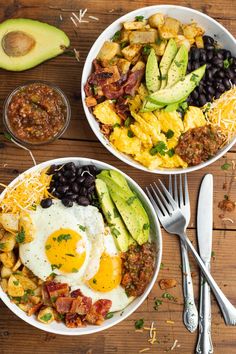 two bowls filled with eggs, beans, avocado and other food on top of a wooden table