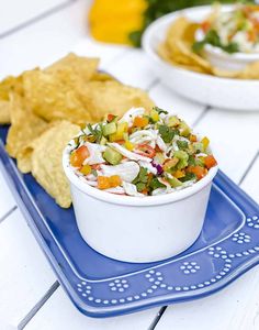 two bowls filled with food sitting on top of a blue tray next to tortilla chips