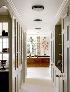 a long hallway leading to a kitchen and dining room with chandelier hanging from the ceiling