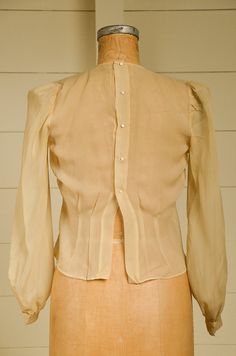 "Antique Silk Blouse Sheer Ivory Button Back Pleated Deco Blouse Beautiful silk blouse. Pleated front with a fitted waistline. Back has metal snap closures with pearl button coverings. Shows normal signs of wear. Measurements shoulders: 13 3/4'' chest: 36\" waist: 33\" length: 20\" sleeve: 23''" Fitted Classic Blouse With Covered Buttons, Classic Formal Blouse With Pearl Buttons, Formal Fitted Blouse With Buttons, Fitted Formal Blouse With Buttons, Formal Fitted Blouse With Back Button Closure, Classic Fitted Blouse With Button Closure, Formal Blouse With Pearl Buttons, Workwear Blouse With Pearl Buttons, Formal Fitted Tops With Pearl Buttons