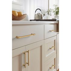 a kitchen with white cabinets and gold pulls on the handles in front of a sink