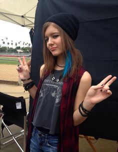 a girl with blue hair is standing in front of a tent and making the peace sign