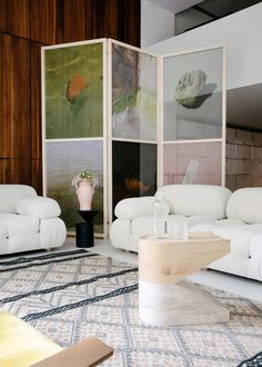 a living room filled with white furniture and art work on the wall behind the couches