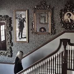 a woman is walking down the stairs in front of pictures on the wall and framed photographs