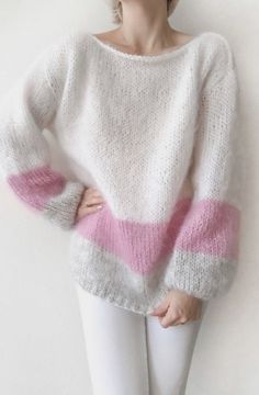 a woman in white and pink sweater leaning against a wall with her hands on her hips