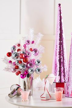 pink and silver christmas decorations on a white table with ornaments in the shape of trees