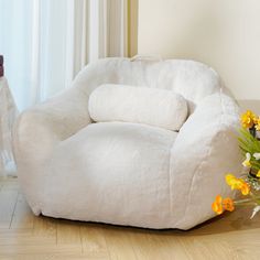 a white chair sitting on top of a hard wood floor next to a vase with yellow flowers