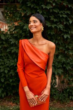 a woman in an orange dress is smiling and holding a gold clutch on her hand