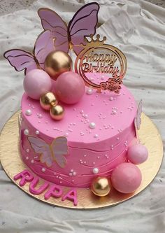 a pink birthday cake with gold decorations and butterflies