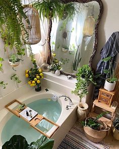 a bathtub with plants in the corner and a mirror above it that is hanging on the wall