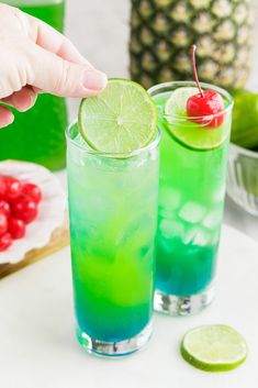 two glasses filled with green and blue liquid next to a pineapple on the table