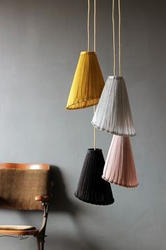 three different colored lamps hanging from a gray wall next to a wooden chair and table