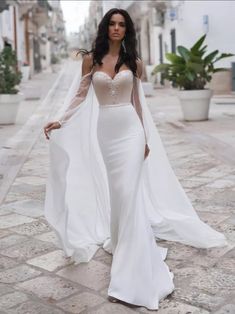 a woman in a white dress is walking down the street wearing a long veil over her head