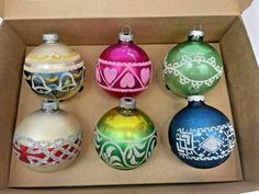 an open box with four different colored christmas ornaments in it's lid and bottom