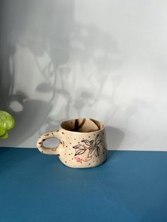 a white cup sitting on top of a blue table next to a green leafy plant