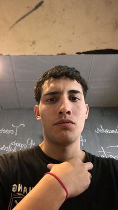 a young man wearing a red bracelet standing in front of a blackboard with writing on it