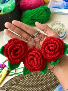 a hand holding two crocheted roses in front of some yarn and knitting needles