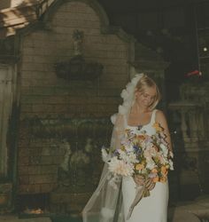 a woman standing in front of a fountain holding a bouquet of flowers and a veil