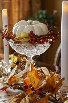 a glass bowl filled with white pumpkins and autumn leaves on top of a table