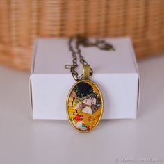 a necklace with an image of a woman in a yellow dress on it sitting next to a white box