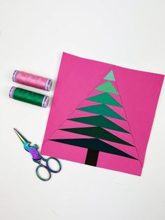 a pink piece of paper with a christmas tree cut out on it next to scissors and spools of thread