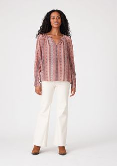 a woman standing in front of a white background wearing a pink blouse and white pants