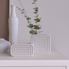 two white vases sitting on top of a table next to each other with plants in them