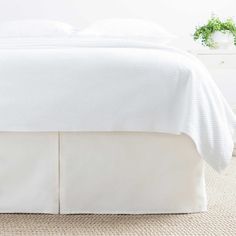 a bed with white sheets and pillows on top of carpeted floor next to window