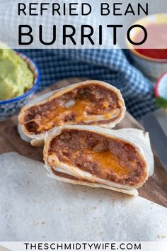 two burritos on a cutting board with guacamole in the background