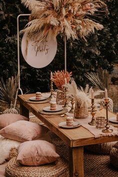 a wooden table topped with lots of pink and gold pillows next to a palm tree