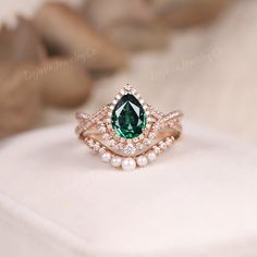 a close up of a ring with a green stone and pearls on the bottom, sitting on a white cloth