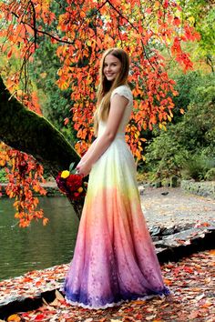 a woman in a long dress standing next to a tree