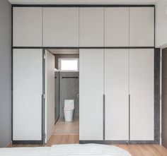 an empty bedroom with white closets and wood flooring on the walls, along with a toilet