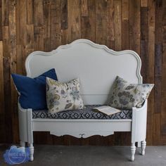 a white bench with pillows on it against a wooden wall