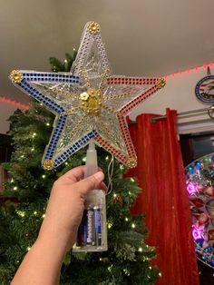 a hand holding a star ornament in front of a christmas tree with red, white and blue lights